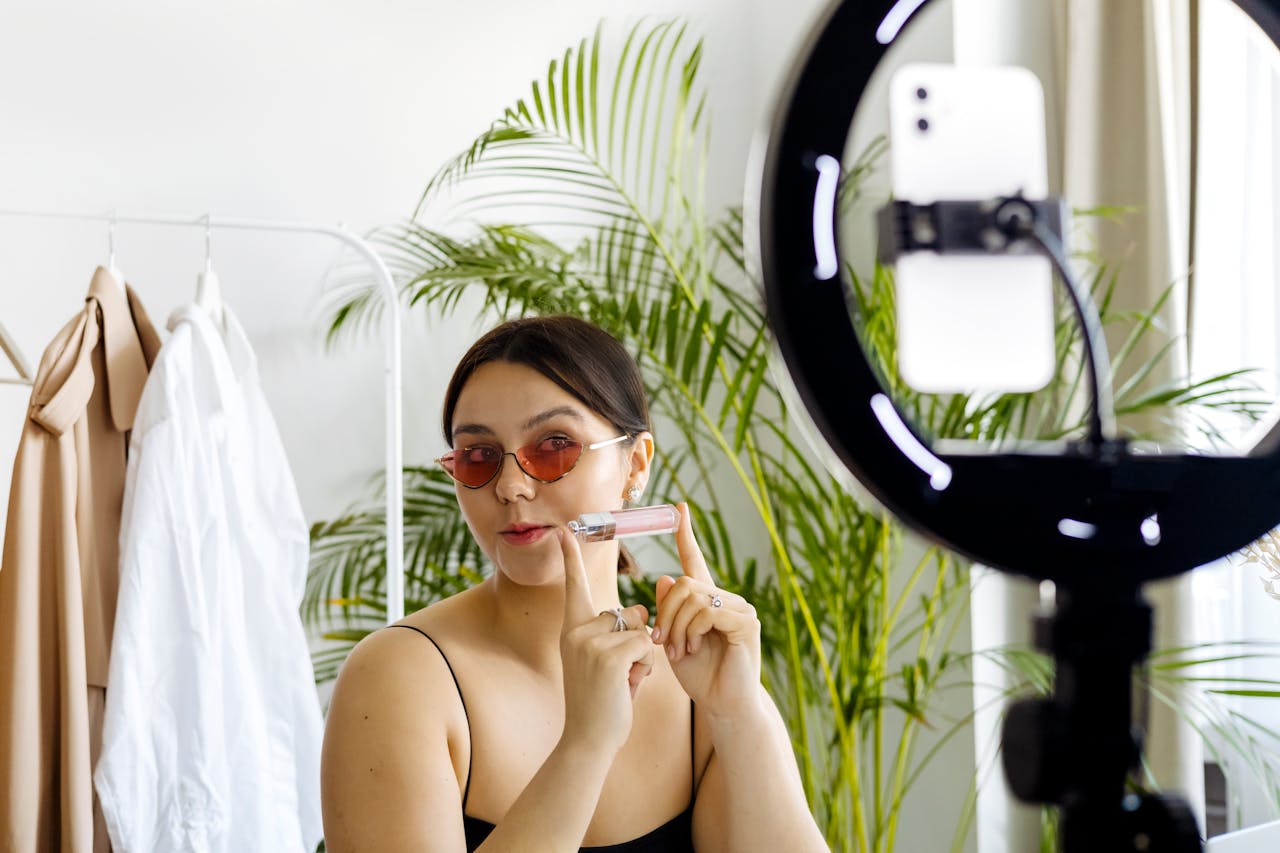 Fashion vlogger showcasing a cosmetic product with a smartphone and ring light setup.